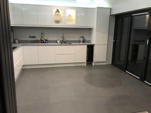 New side extension incorporating white high gloss handless kitchen , Bi-fold doors leading to garden & grey porcelain floor tile