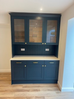 A traditional style wood grained kitchen with a contemporary twist , incorporating quartz worktops , flush recessed ceramic hob , butler style sink with Quooker tap , integrated double ovens , wine fridge housed within the island & stand alone bespoke dresser.